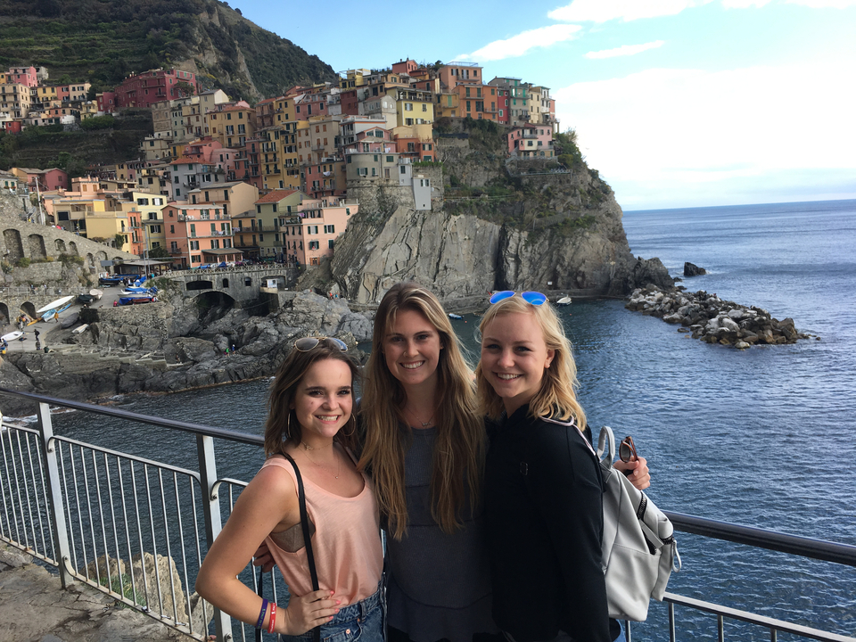 Trois femmes posant ensemble le long de la côte avec des bâtiments vibrants à flanc de colline.