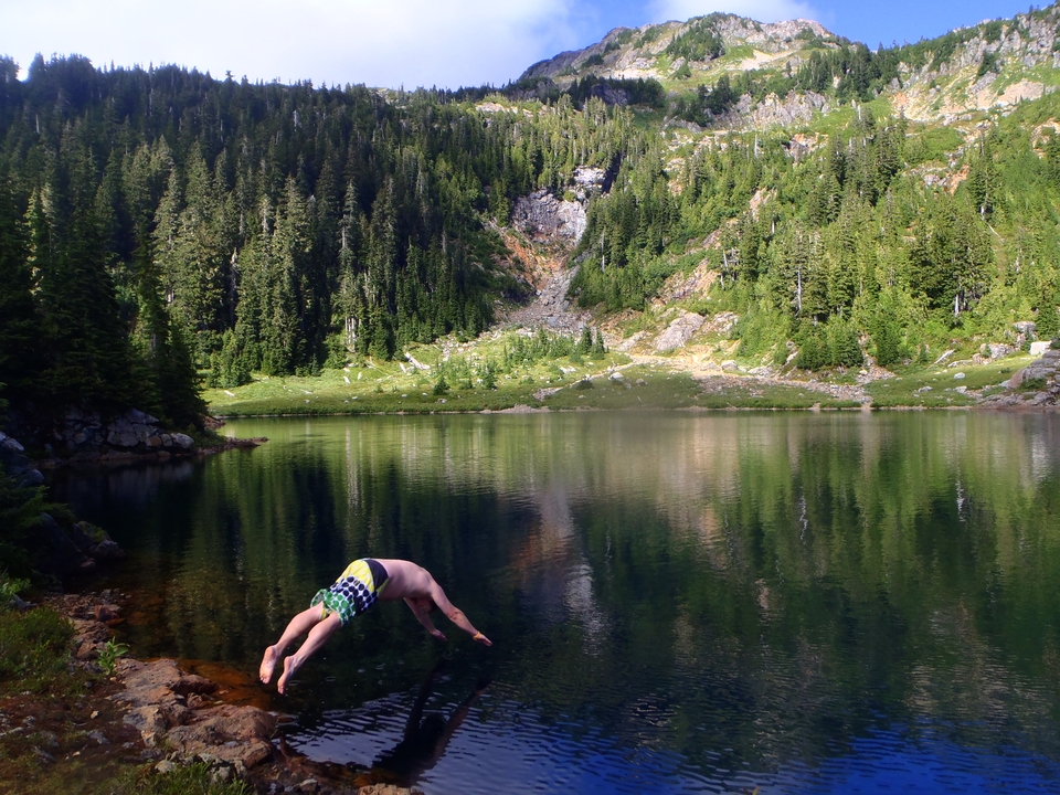 Personne plongeant dans un lac clair entouré de forêts.