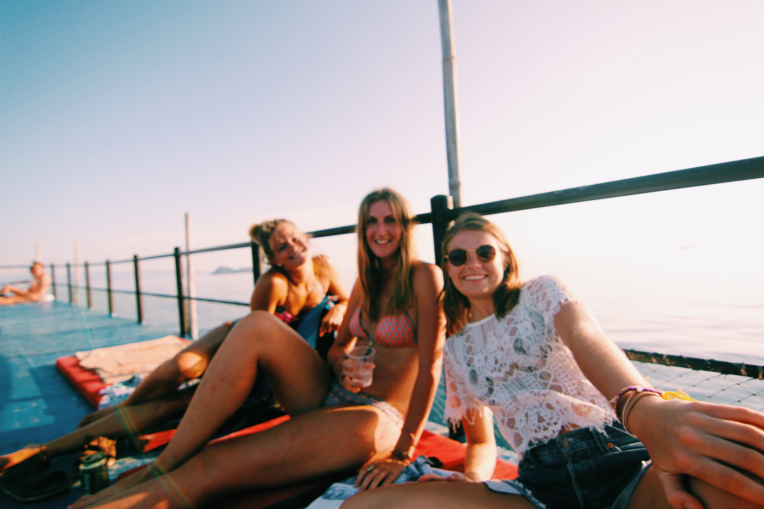 Three women smiling on a deck near the ocean.