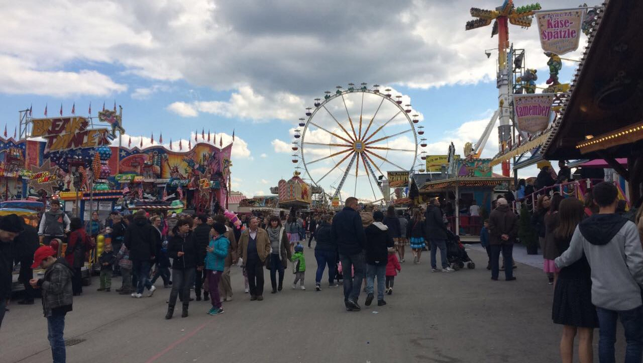 Fête foraine bondée avec une grande roue et des stands.