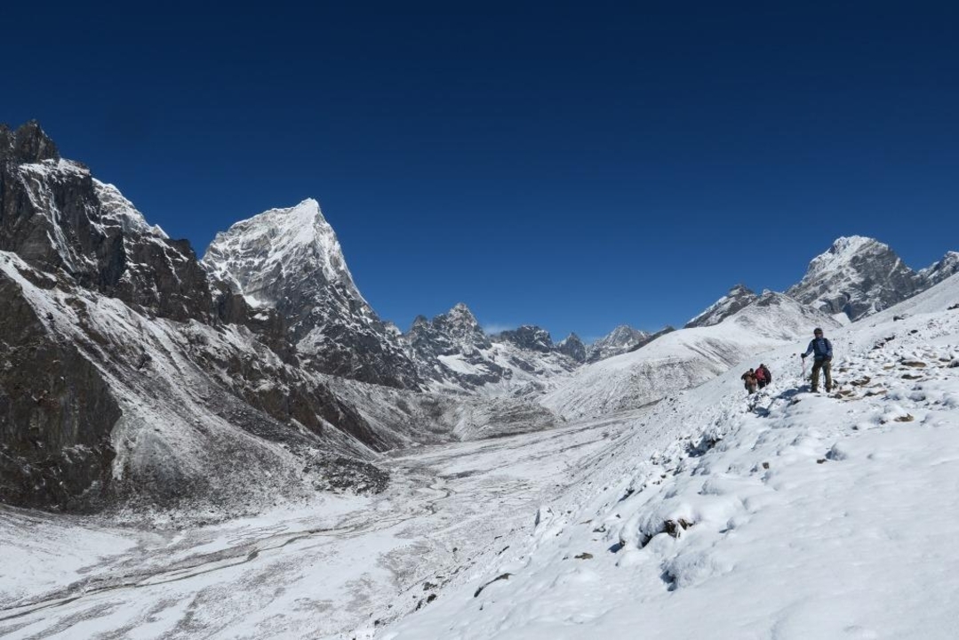 Wide snow-covered valley with trekkers and a mountain backdrop.