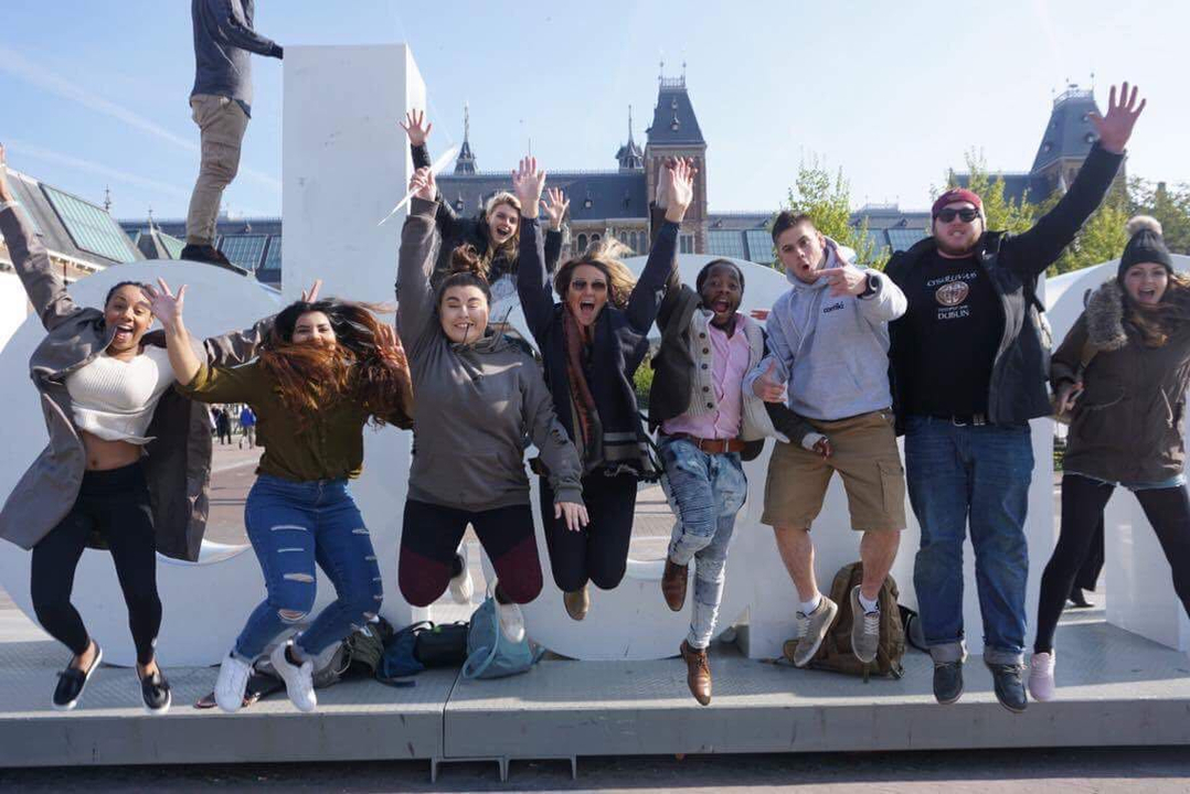 Groupe de touristes sautant devant de grandes lettres dans une ville.