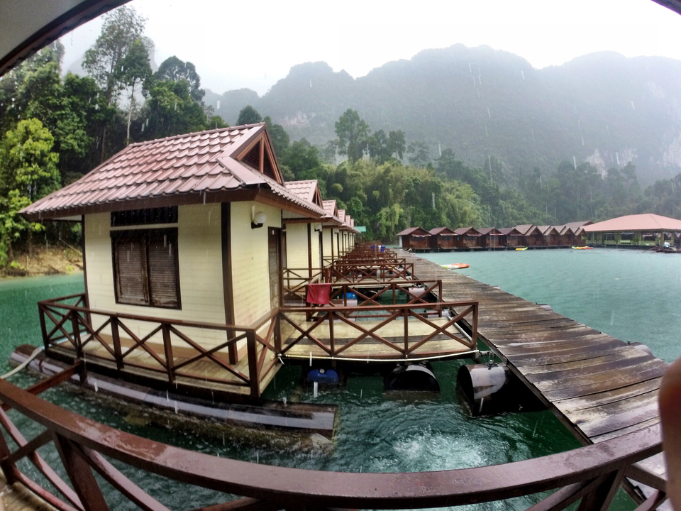 Stilted cabins over water in a forested area under cloudy sky.