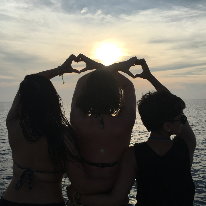 Three people forming heart shapes with hands at sunset over the sea.