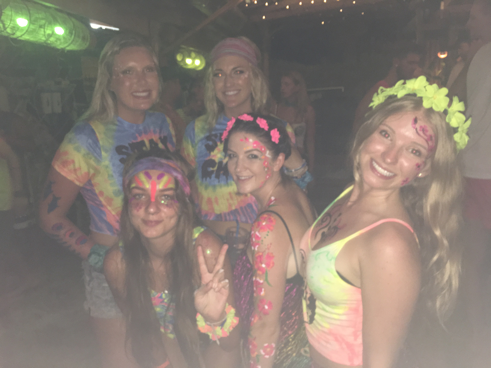 A group of people in brightly colored outfits with painted faces at night.