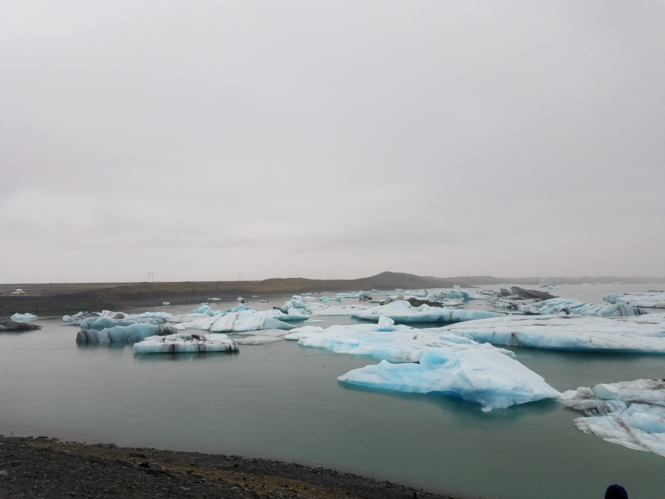 Icebergs of pale blue ice float quietly in a glacial lagoon beneath a grey sky.