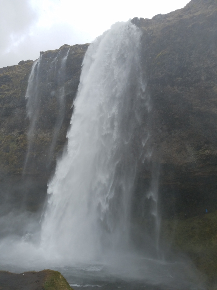Tight crop of a powerful waterfall dropping against dark mossy cliffs.