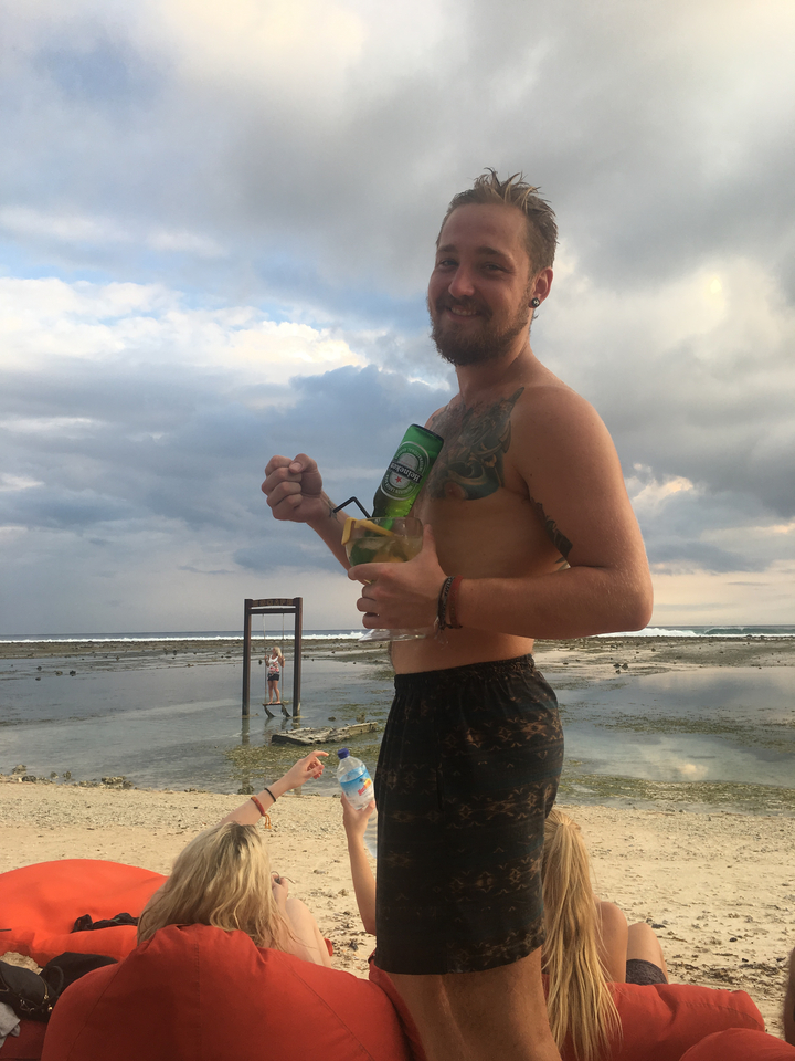 Man holding drinks at a beach setting.