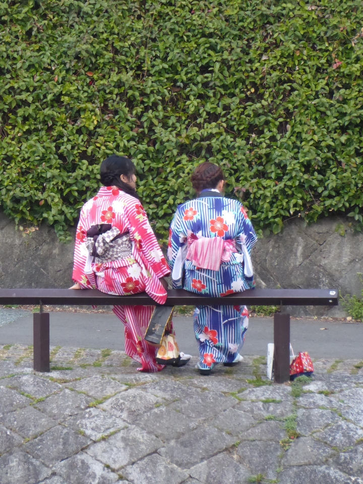 Two women in traditional kimonos sitting on a bench.