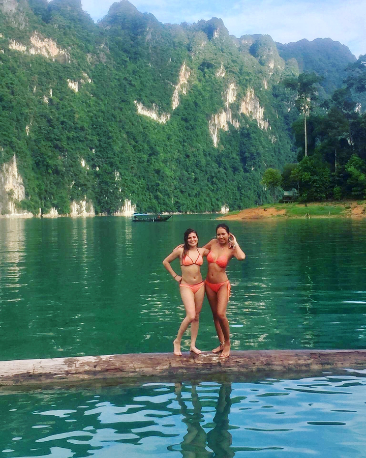 Two women standing in shallow water near a lush shoreline.