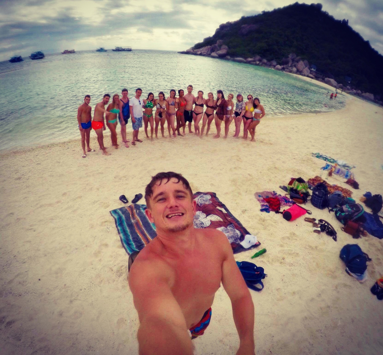 Group of people posing on a beach with blankets and bags laid out on the sand.
