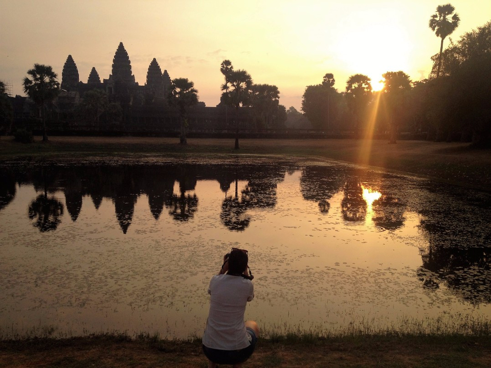 Photographe prenant une photo du lever de soleil se reflétant sur un étang avec Angkor Wat en arrière-plan.