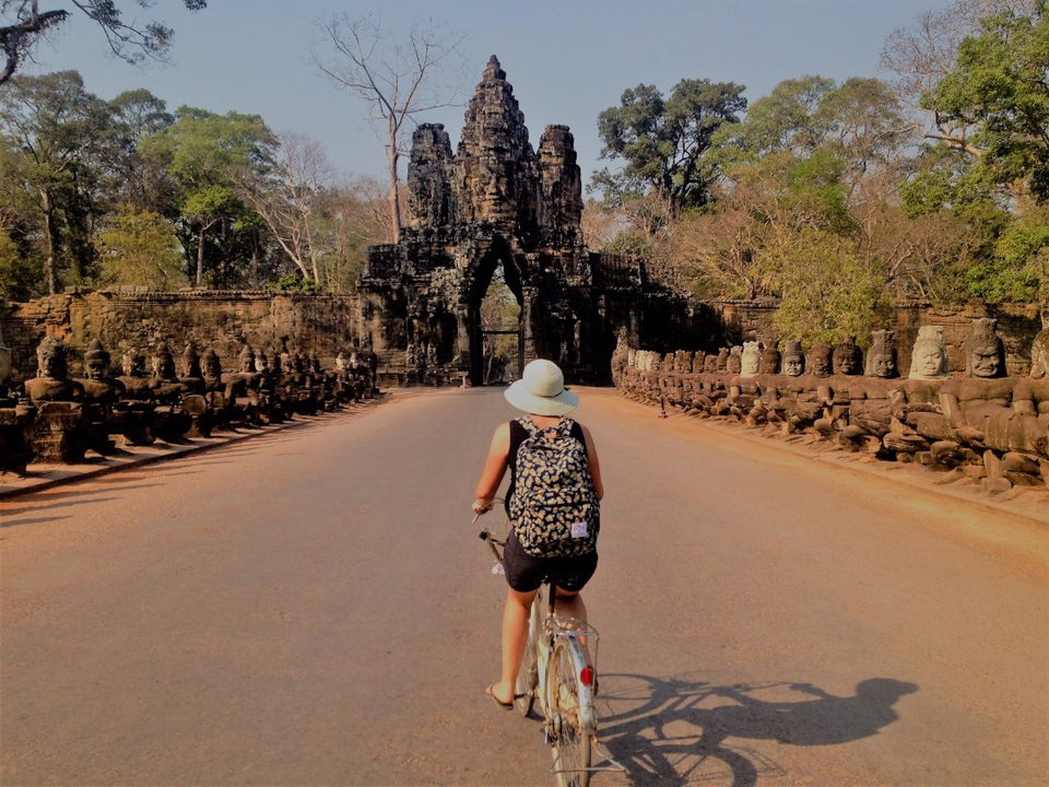Cycliste s'approchant des anciennes portes d'Angkor Thom flanquées de statues.