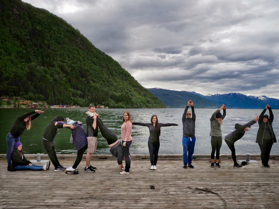 Groupe de personnes posant de manière créative sur un quai au bord d'un lac avec des montagnes en arrière-plan.