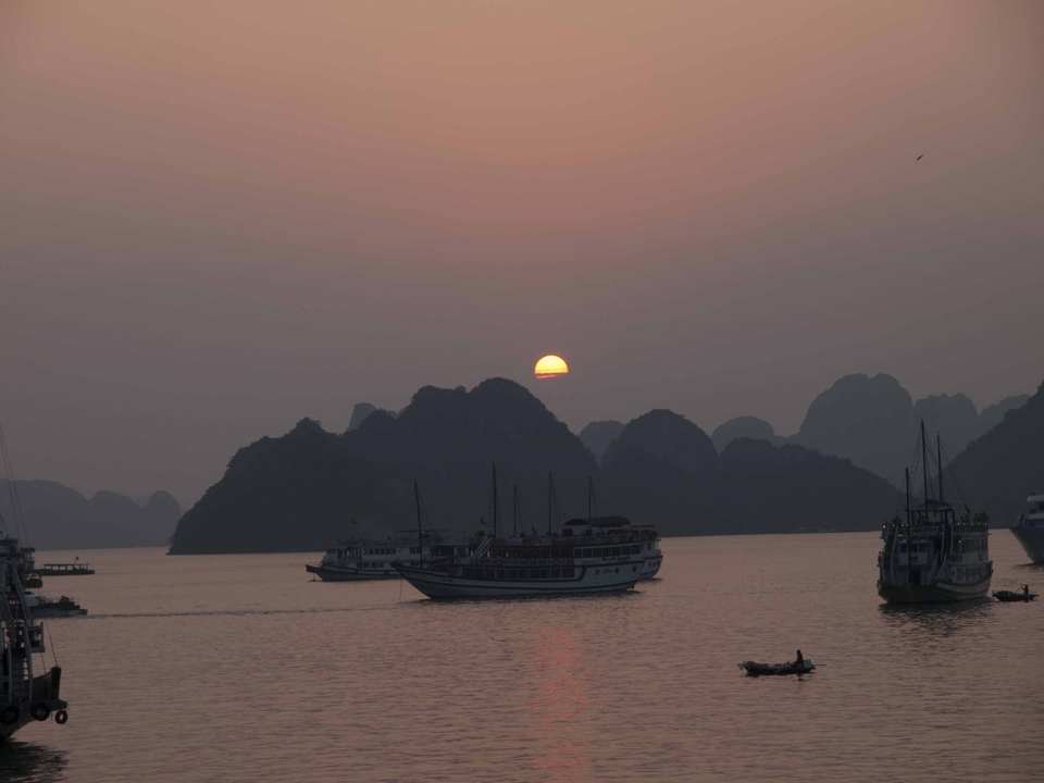 Bateaux naviguant sur une baie brumeuse au coucher du soleil.
