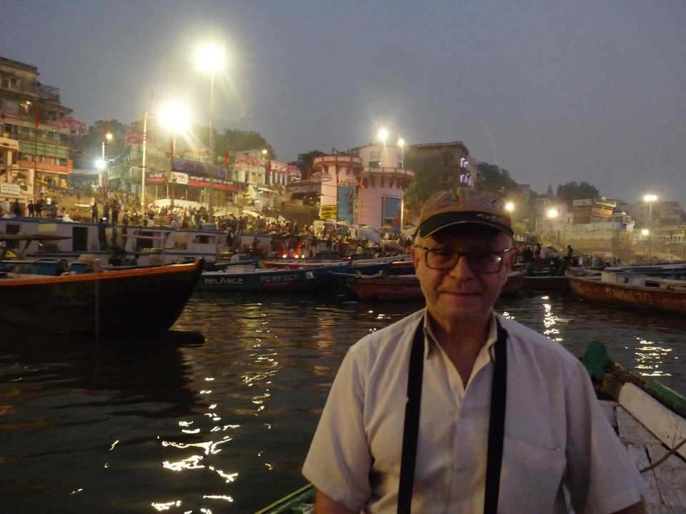 Personne debout au bord d'une rivière avec des bâtiments et des bateaux illuminés.