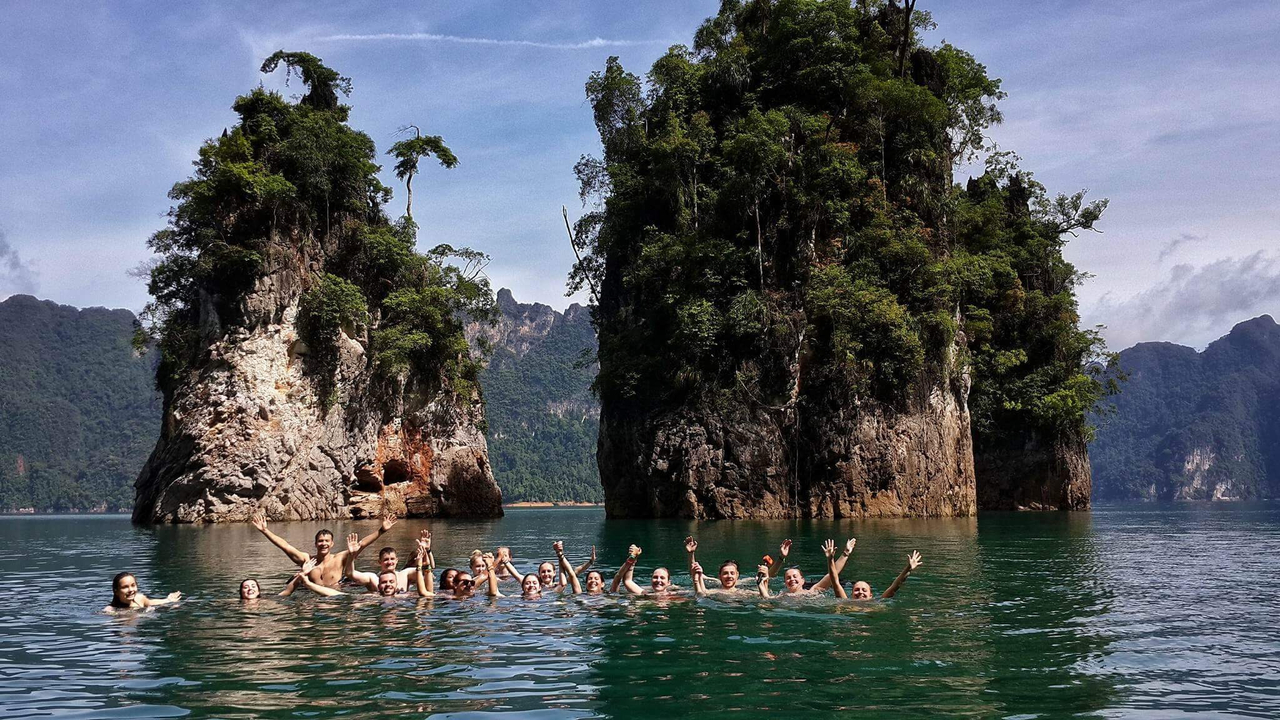 Group of people swimming in a lake with tall rock formations.