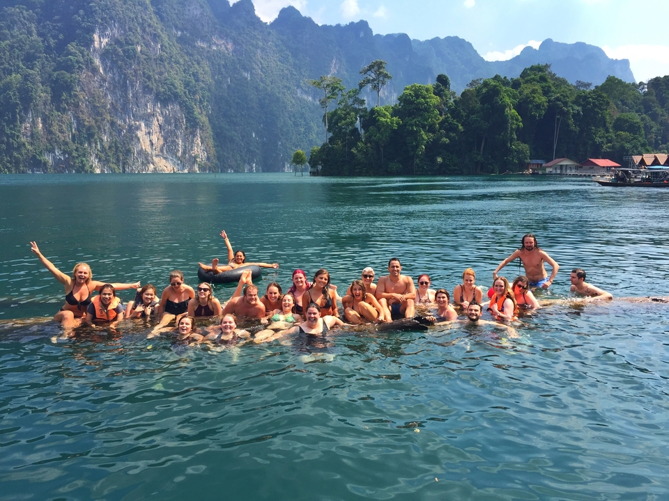 Grand groupe de personnes nageant dans un lac clair avec des collines verdoyantes.