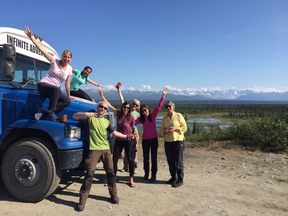 Groupe de personnes posant près d'un bus bleu avec des montagnes en arrière-plan.