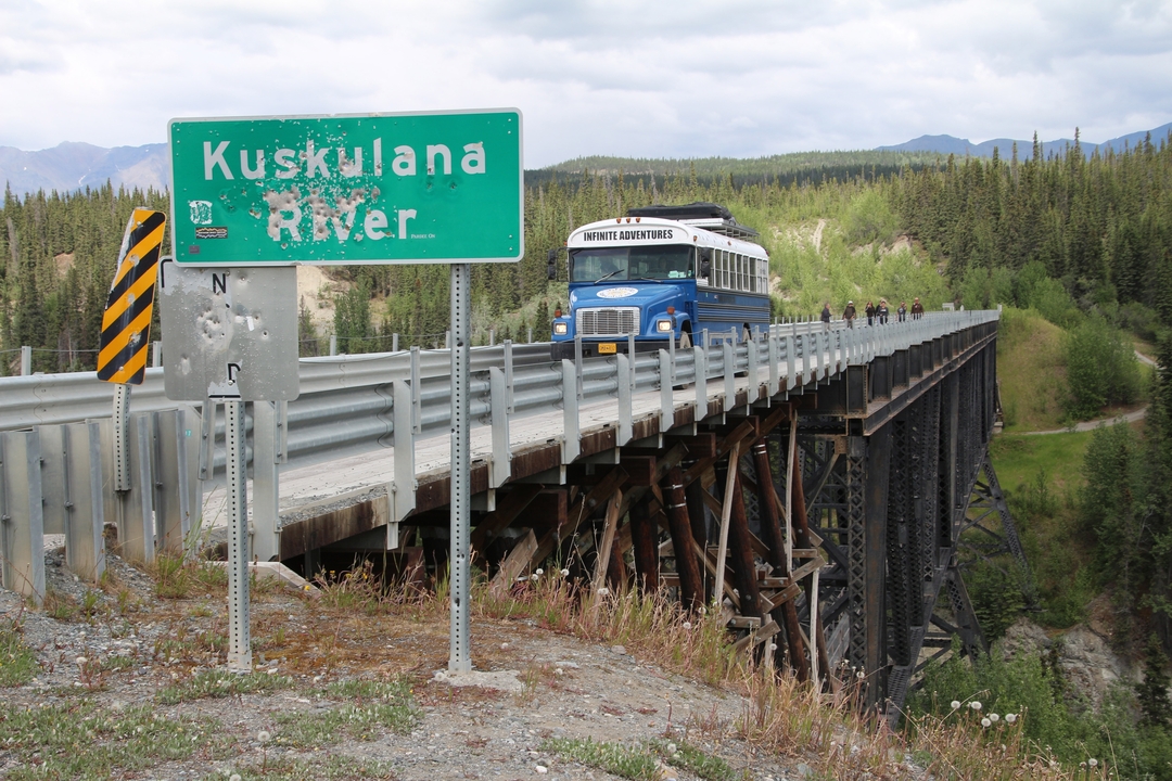 Pont avec un bus touristique et un panneau indiquant la rivière Kuskulana.