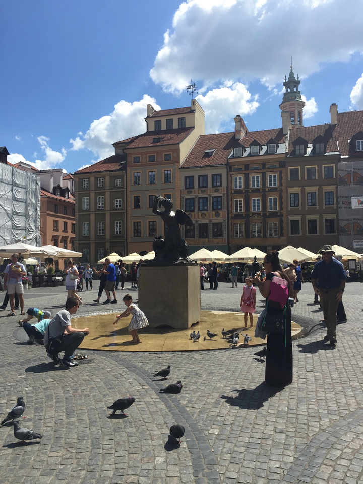 Place du marché avec une fontaine entourée de bâtiments et de personnes.