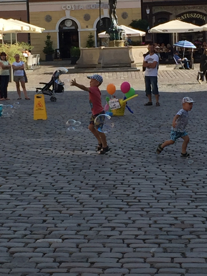 Enfants jouant avec des bulles dans une rue pavée.
