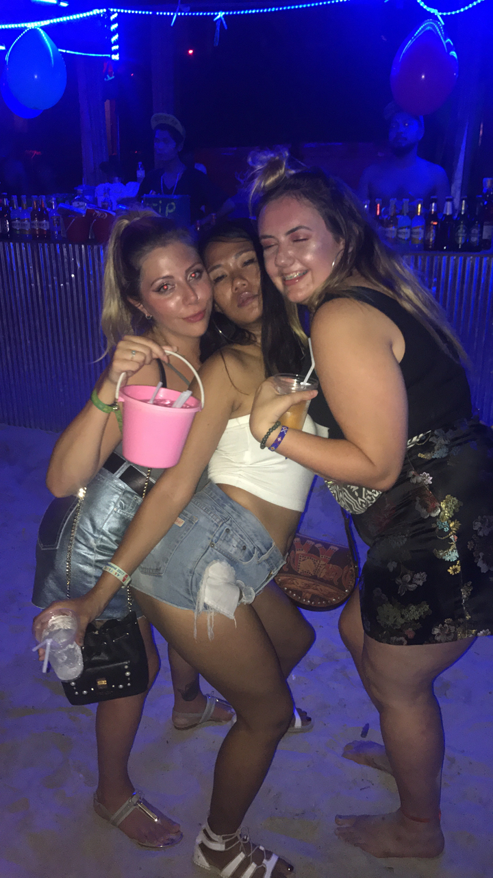 Three people posing with drinks in their hands at night.