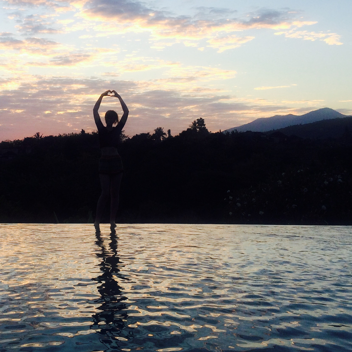 Silhouette of a person making a heart shape with hands during sunset.
