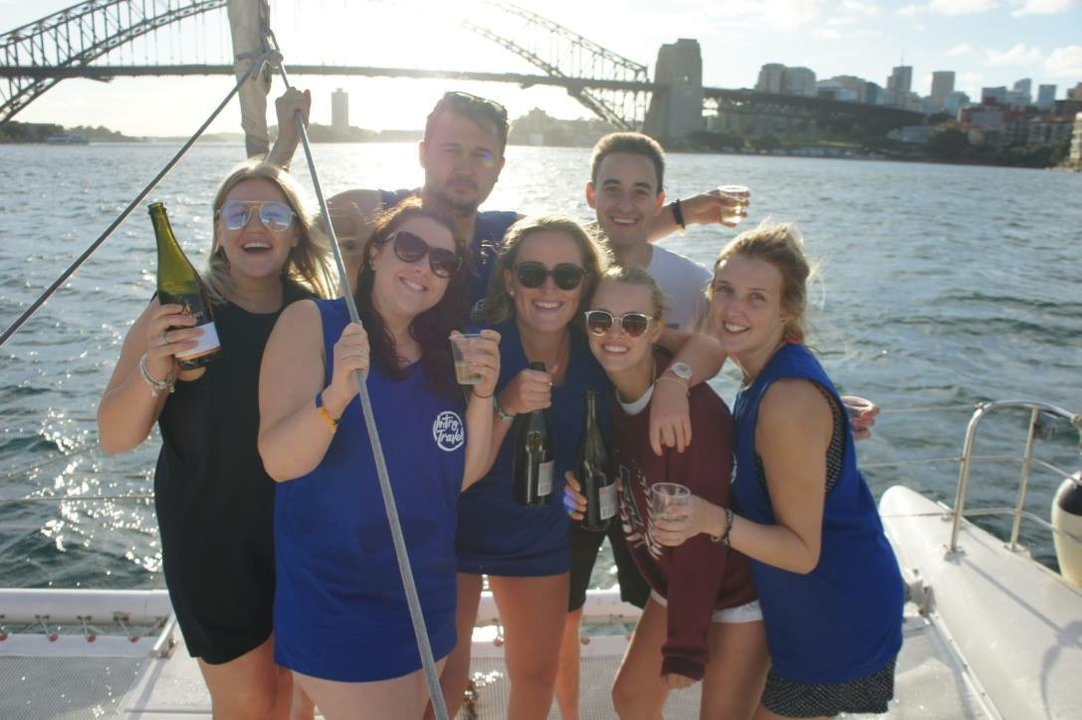 Group of friends on a boat enjoying drinks with a bridge in the background.