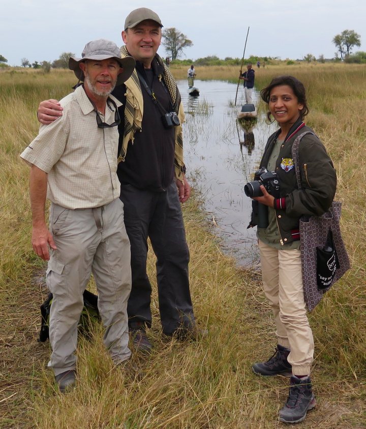 Trois personnes posant avec des jumelles et des appareils photo dans une zone herbeuse.