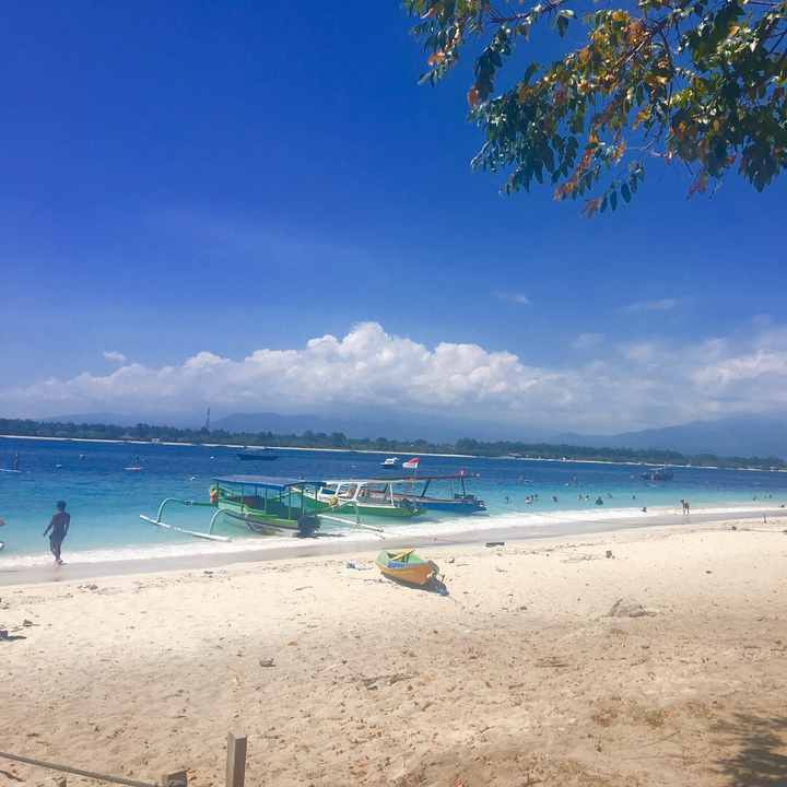 Clear blue water and a sandy beach with boats in the distance.