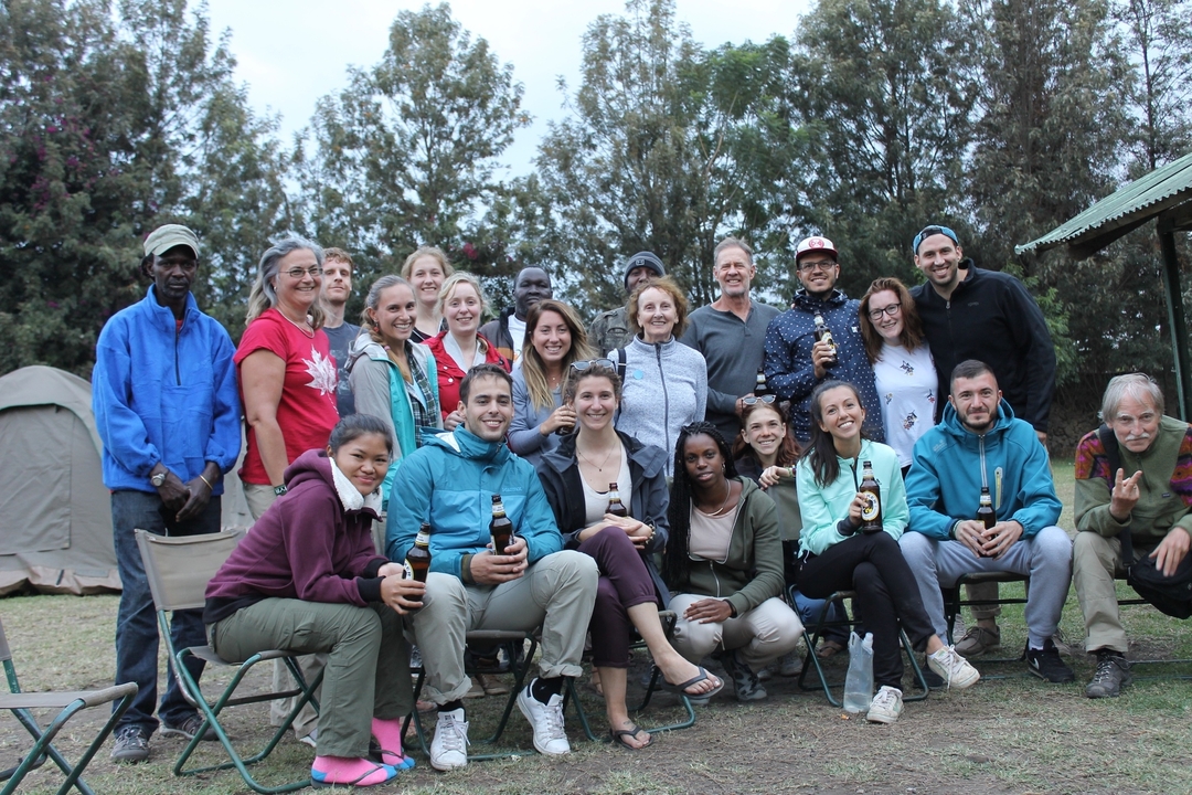 Grand groupe de personnes rassemblées en plein air, certaines tenant des bouteilles.