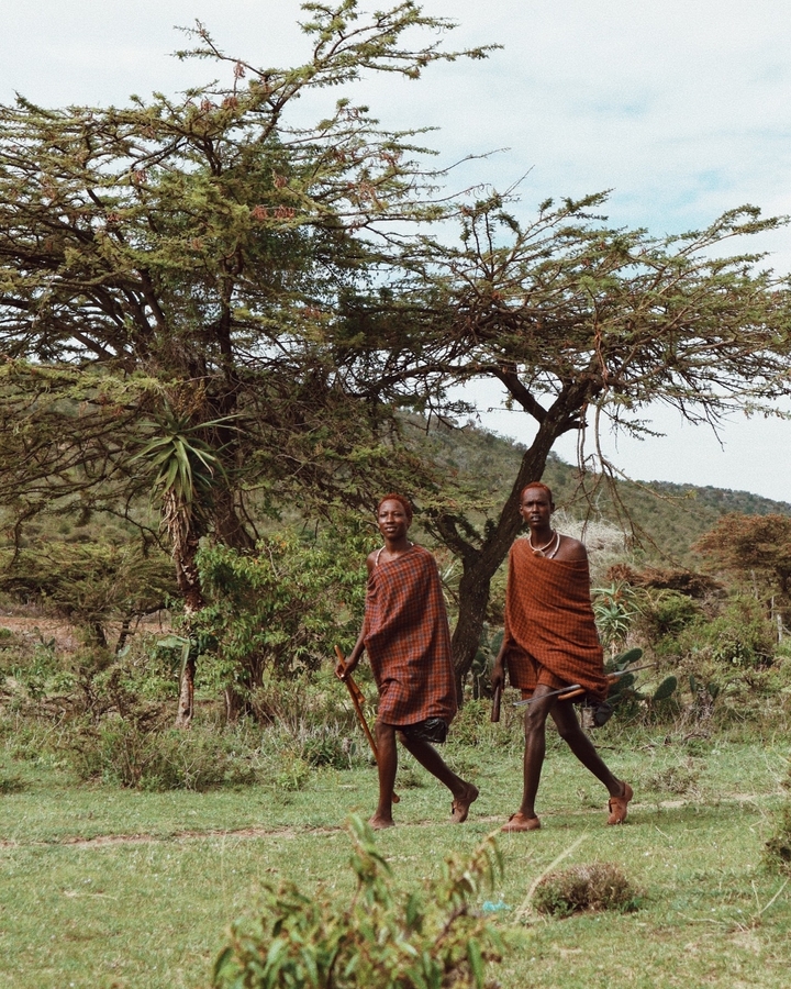 Deux hommes masaïs debout sous des arbres, en tenue traditionnelle.