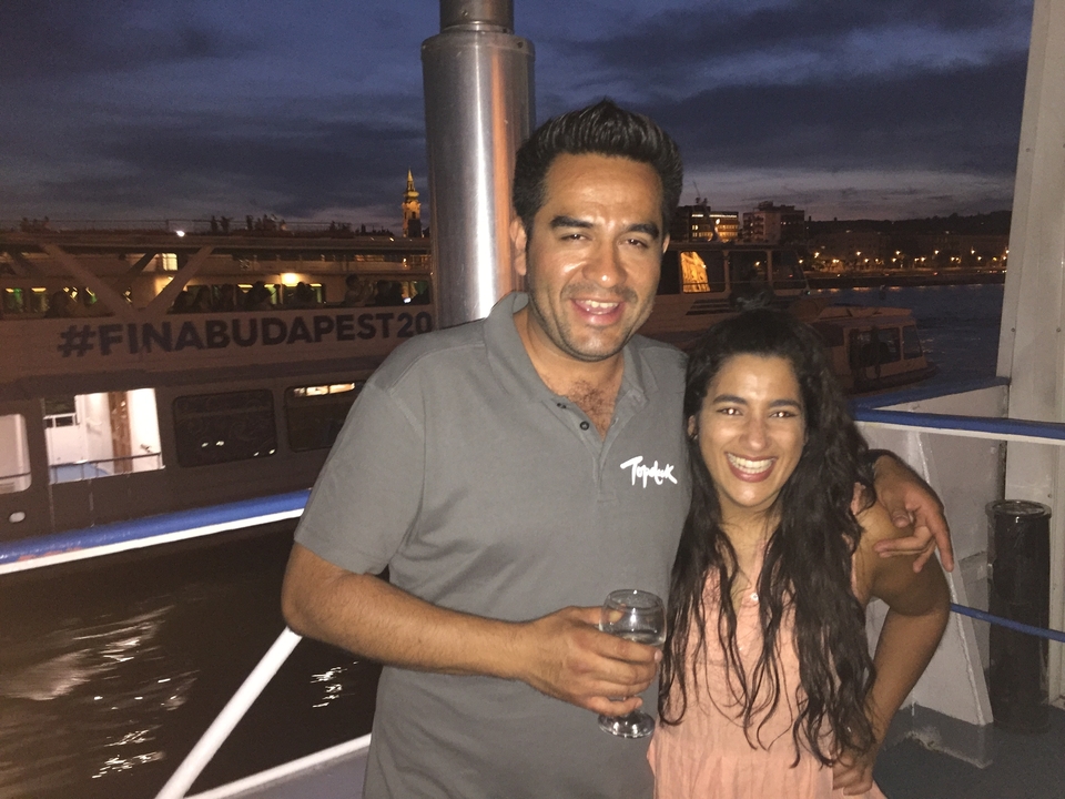 Deux personnes souriant sur un bateau sous les lumières de la ville, avec une bannière en arrière-plan.