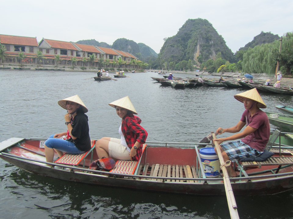 Touristes dans un bateau traditionnel sur une rivière pittoresque avec des montagnes.