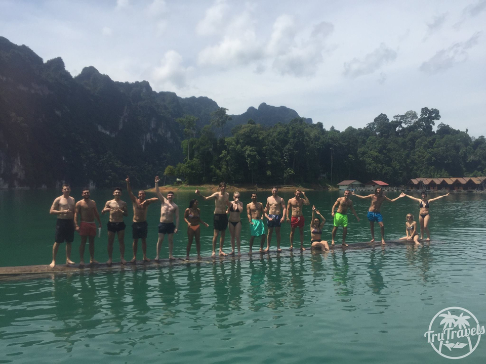 Group of people standing on a log over water.