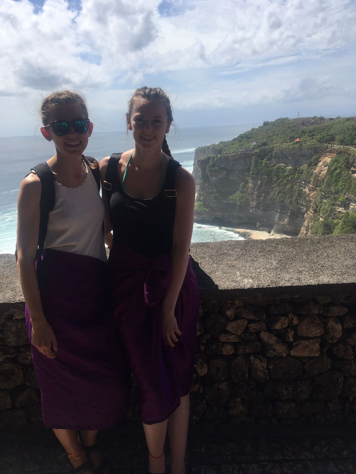 Two women posing with a scenic cliff backdrop.