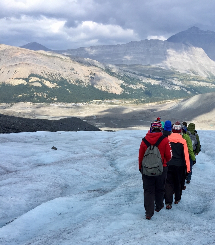 Personnes marchant sur un glacier avec un arrière-plan montagneux.
