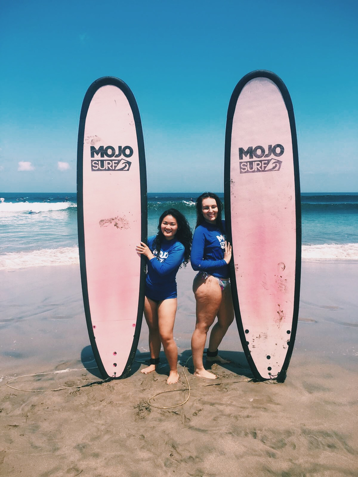 Two women posing with surfboards on a beach.