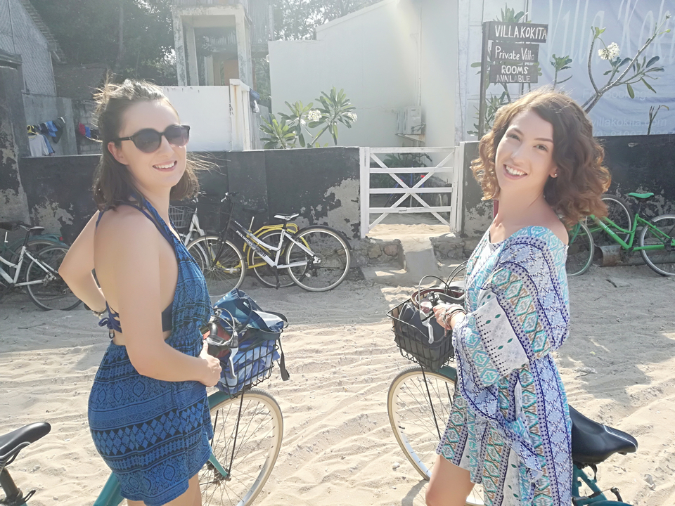 Deux femmes souriant sur des bicyclettes dans un cadre ensoleillé.