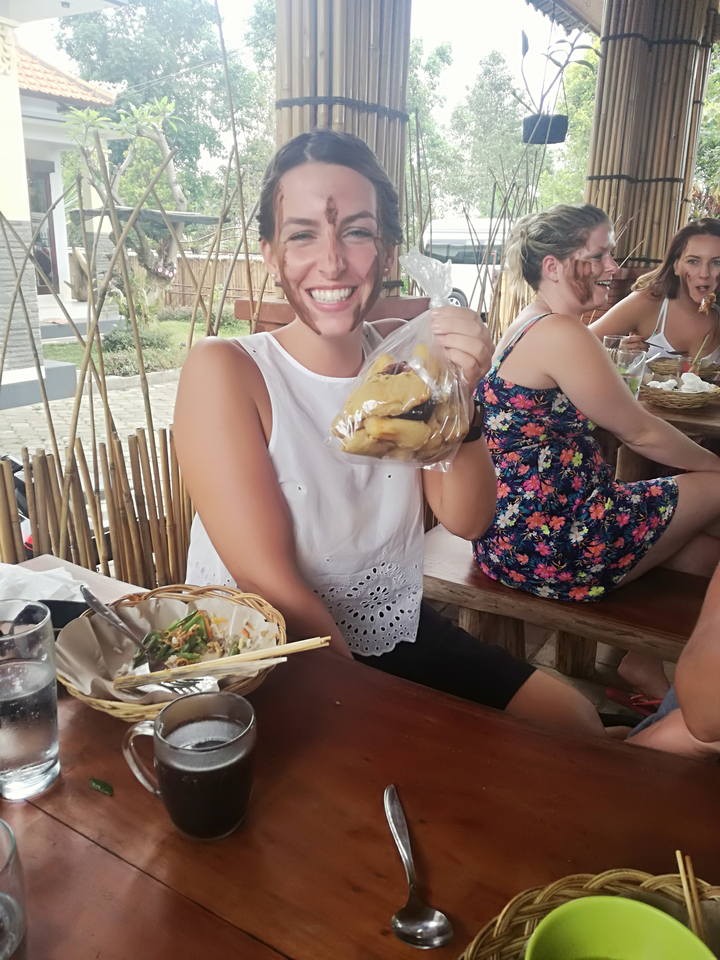 Une personne tenant un sac de fruits, assise dans un restaurant en plein air avec un plat sur la table.