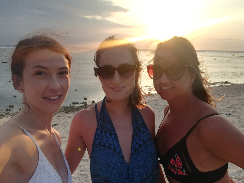 Trois femmes portant des lunettes de soleil sur la plage au coucher du soleil.