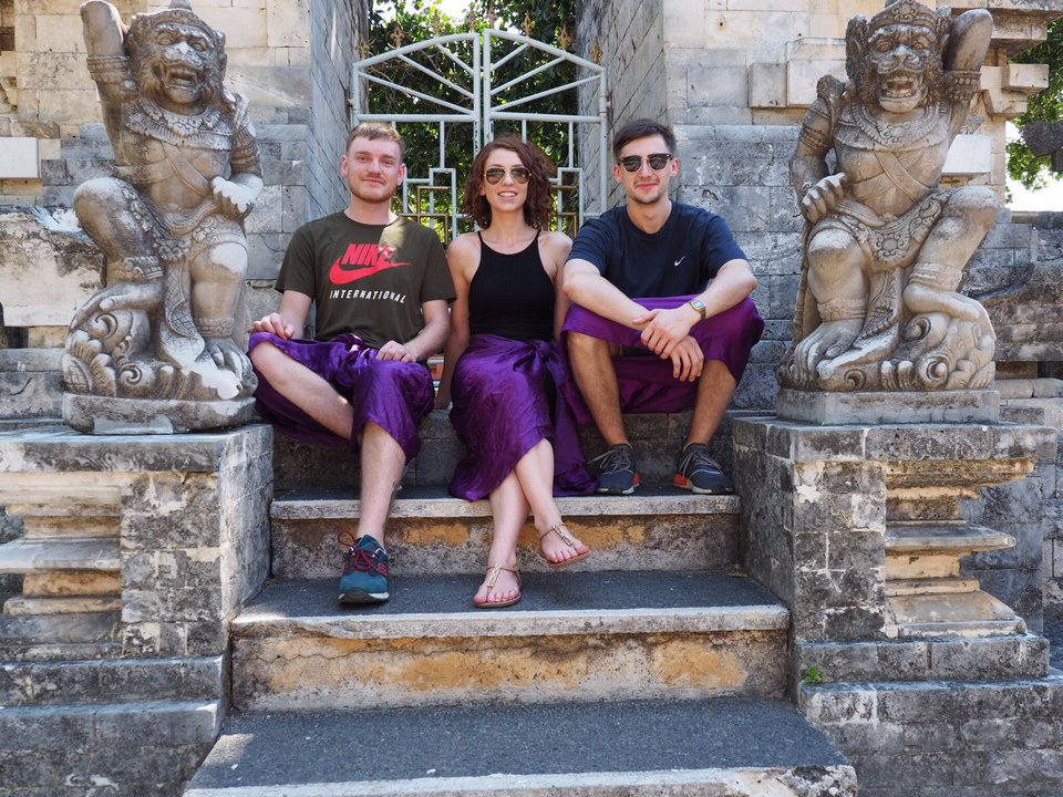 Trois personnes assises sur des marches en pierre à côté de sculptures traditionnelles.