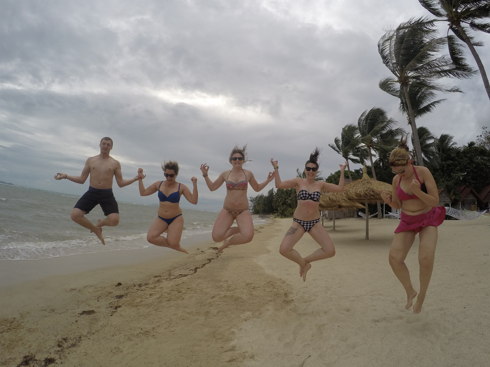 Group of people jumping on a beach with palm trees.