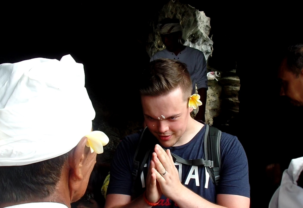 A man in a cultural ritual with a flower behind his ear.