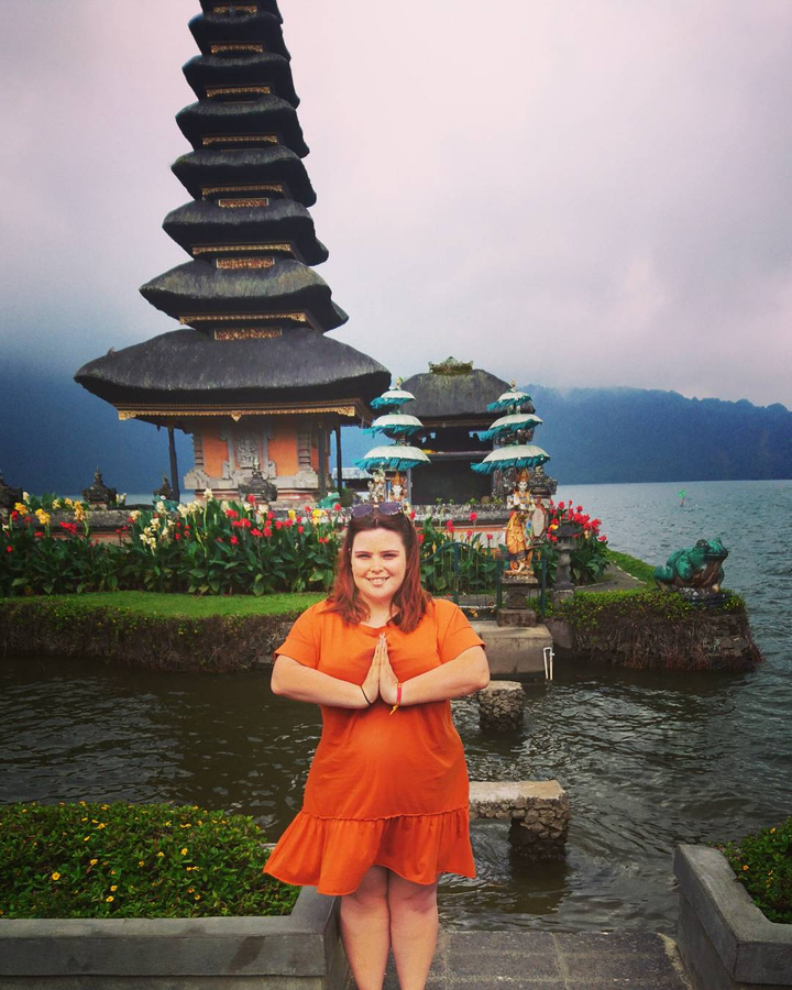 Woman posing in front of temple structures by a lake.