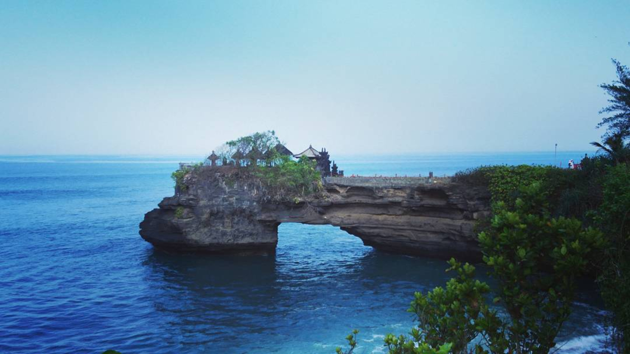 Ocean view with rock arch formation and temple.