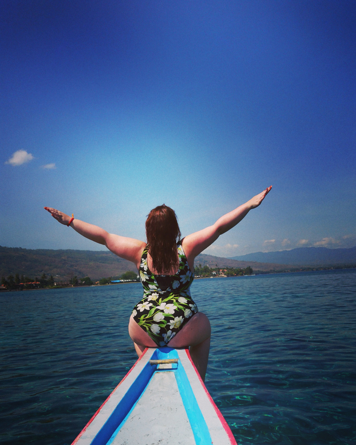 Woman with arms outstretched standing on a boat in the sea.