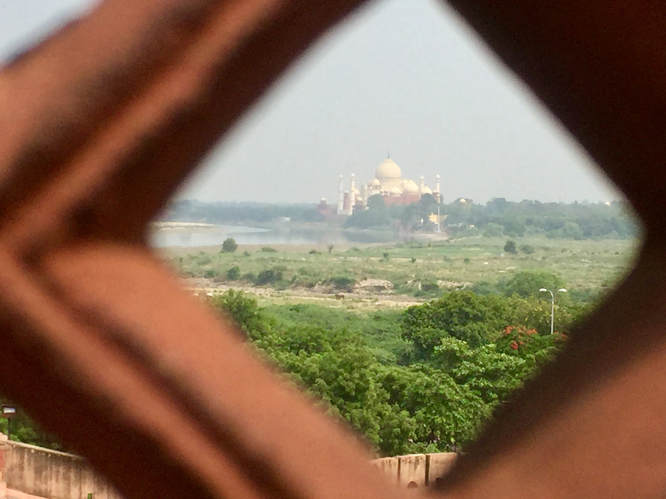 Vue lointaine du Taj Mahal depuis une fenêtre décorée.