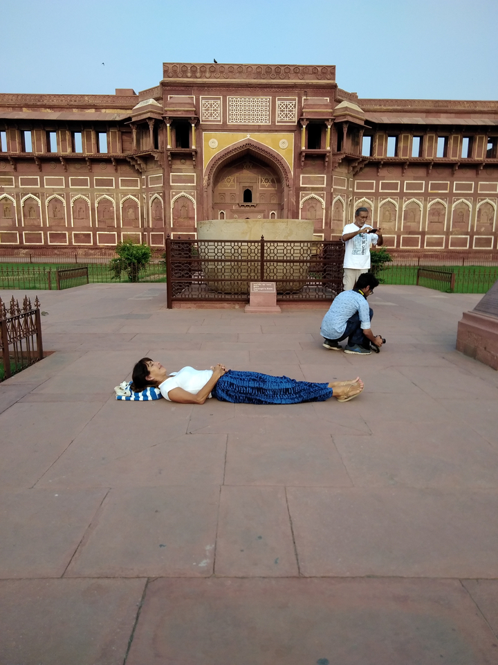Personne allongée dans une cour historique, tandis que d'autres personnes prennent des photos.